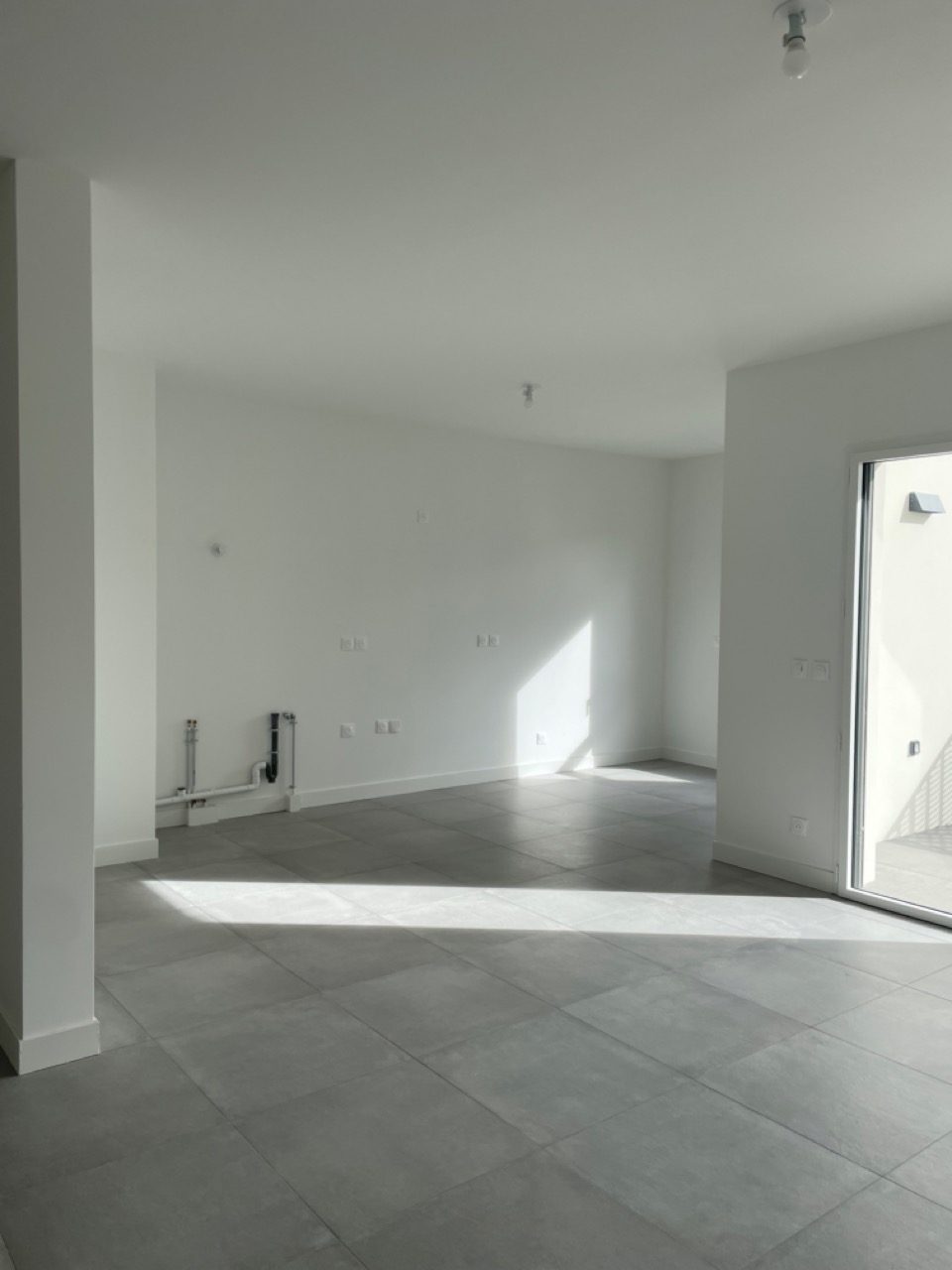 Avant : la pièce de vie neuve, murs blancs et carrelage gris, appartement dans le 9e à Lyon