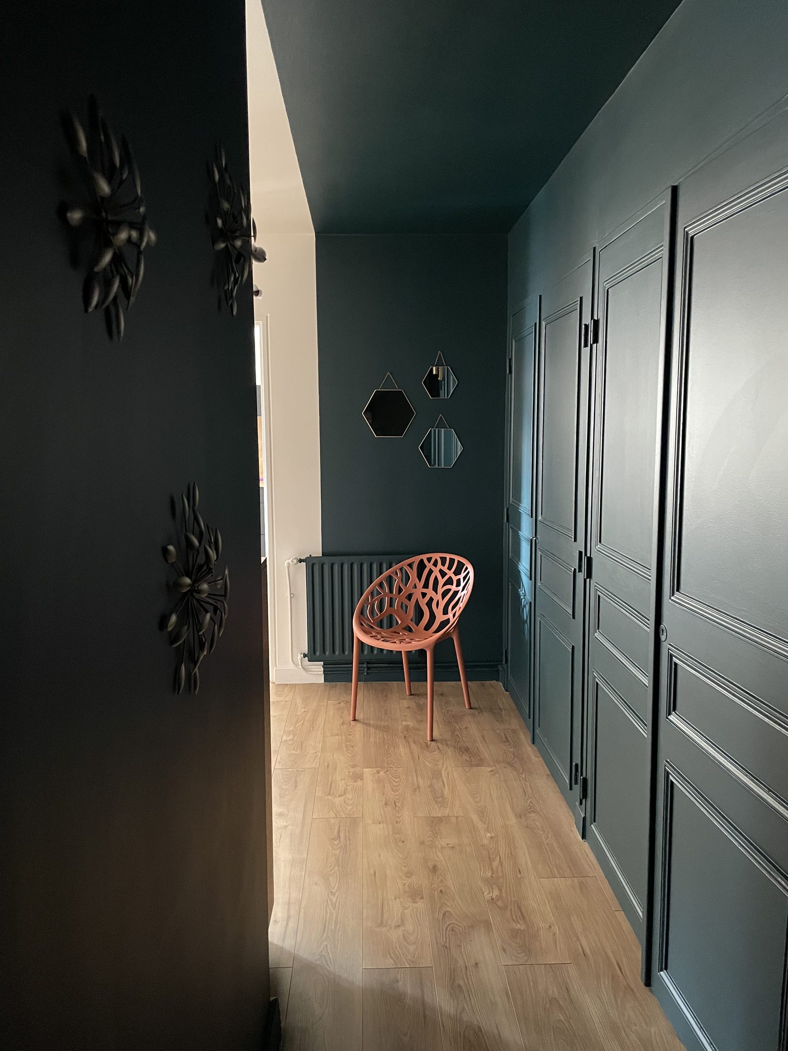 Couloir en vert profond avec placards à moulures, chaise terracotta ajourée et miroirs hexagonaux, appartement à Villefranche