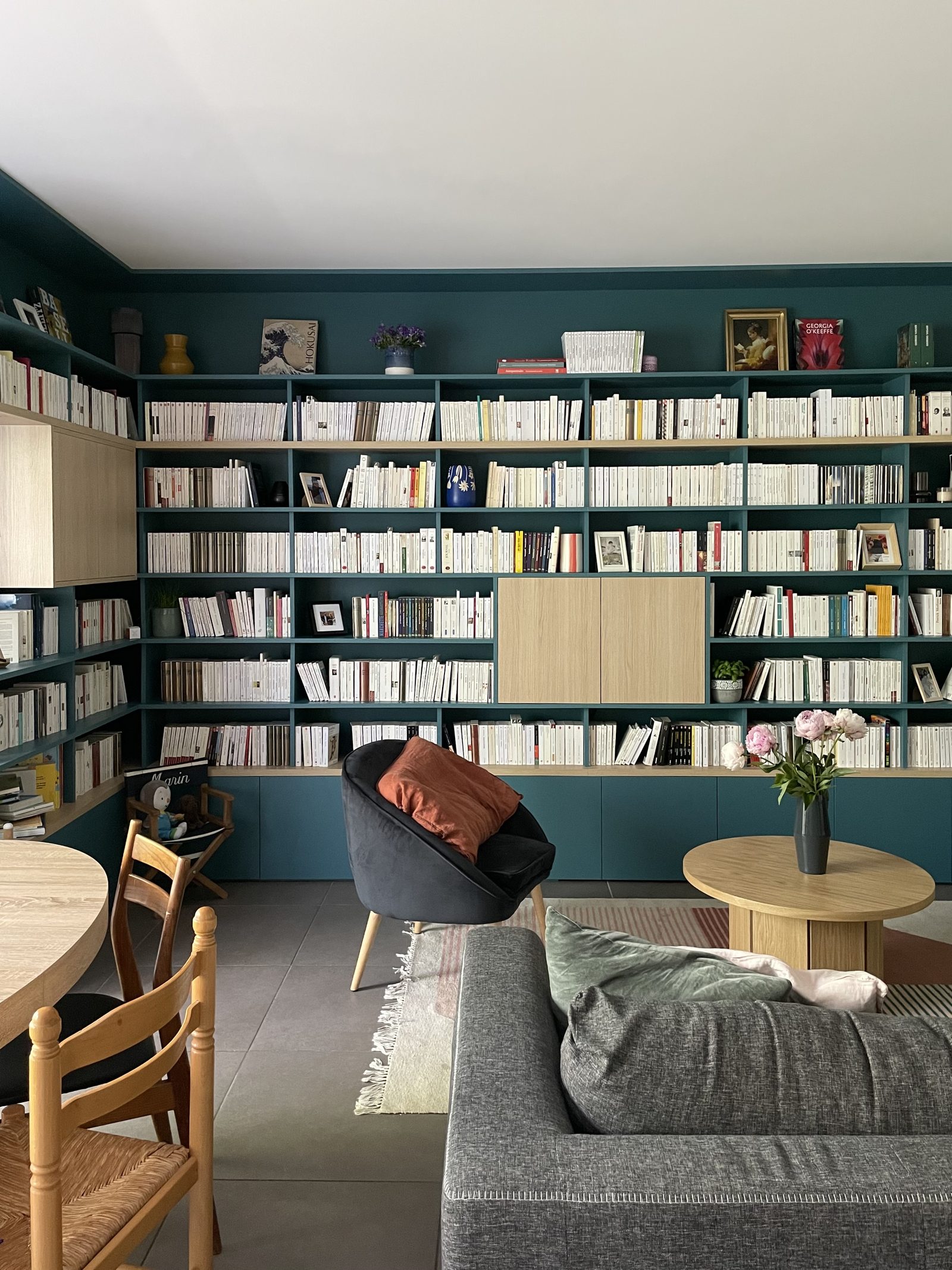 Coin lecture avec canapé, table basse ronde et pivoines devant la bibliothèque bleu canard, projet Teppaz