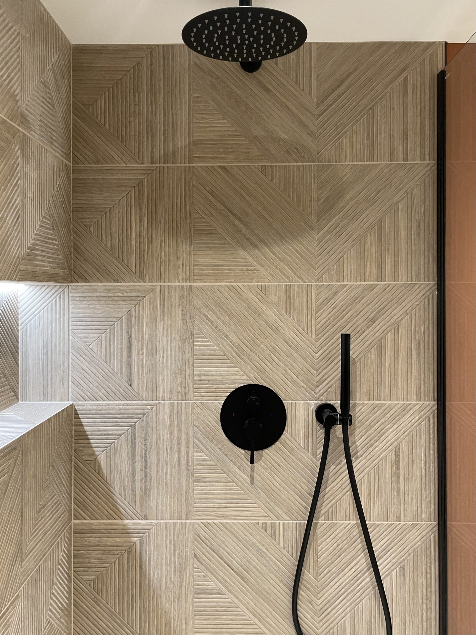 Détail de la douche : carrelage effet bois en chevron, niche rétro-éclairée et robinetterie noire, projet Viala à Montchat